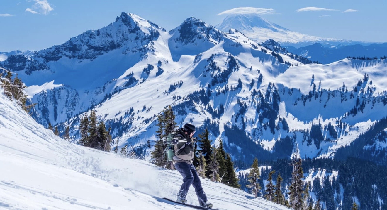 Skier descending a snowy slope with Mount Rainier in the distance